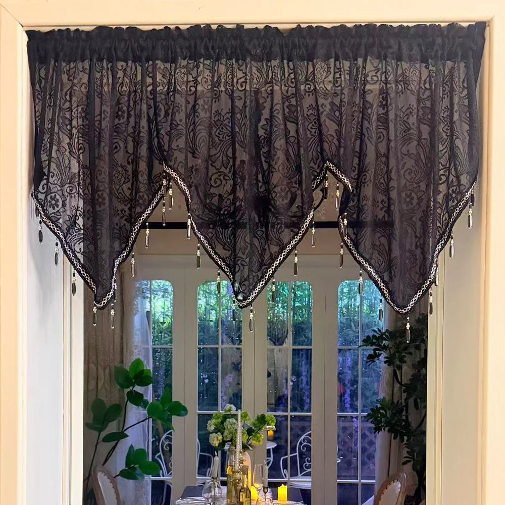 Black lace curtain valance with silver pendants framing a window in a home setting.