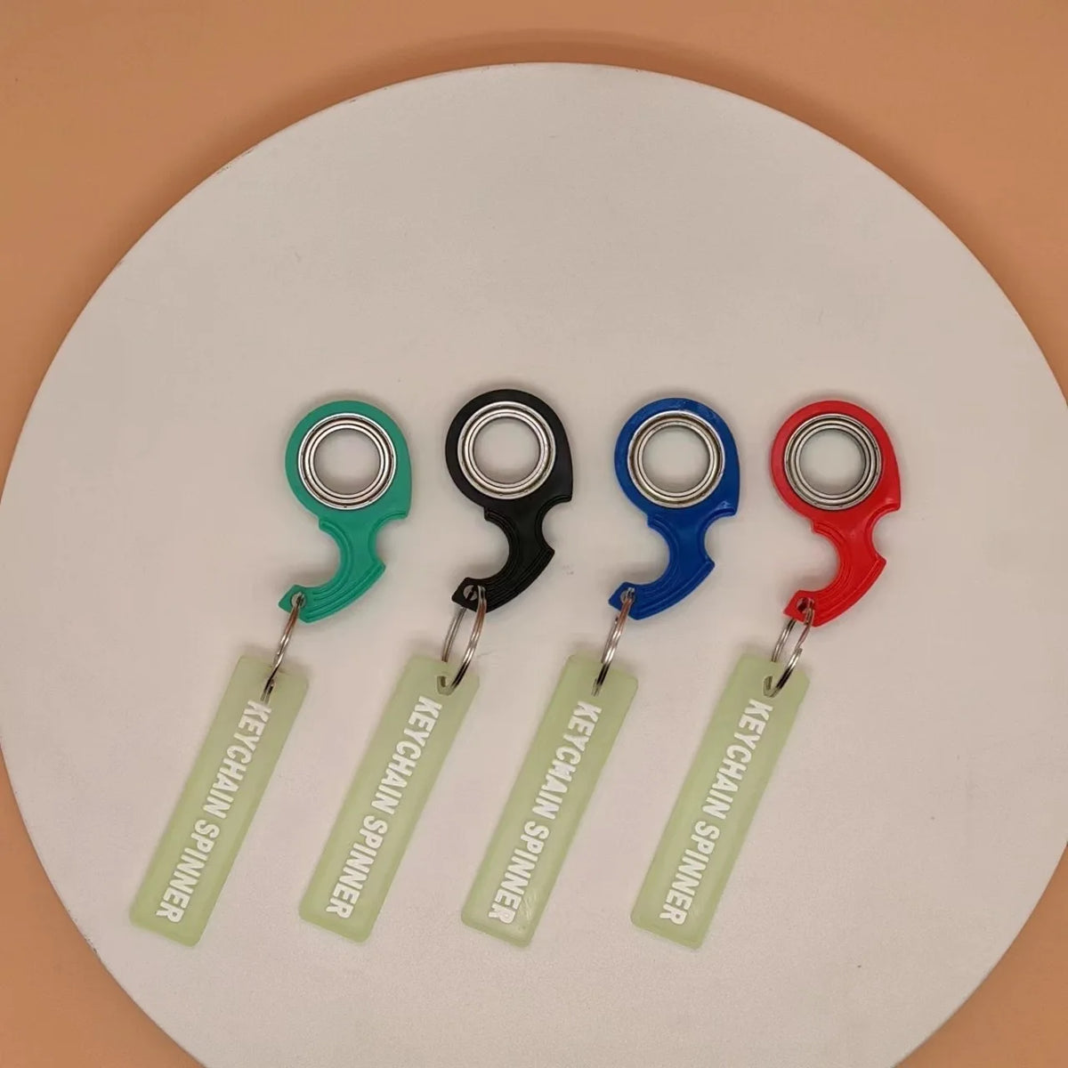 Five metal fidget spinner keychains in green, black, blue, and red on a white background.