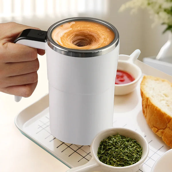 A hand holds a white mug with a silver lid containing latte art, placed on a tray next to a small bowl of green tea leaves.