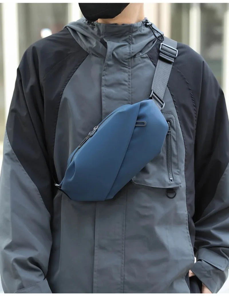 A man wearing a gray waterproof jacket has a navy blue running waist pack attached to his chest.