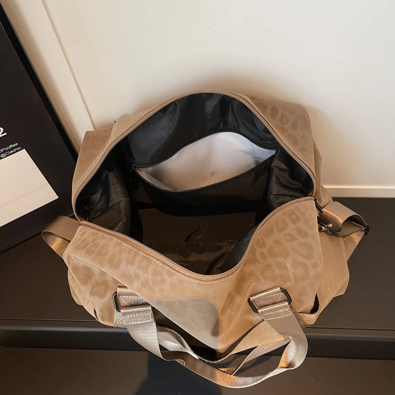A tan leopard print duffle bag with adjustable straps resting on a dark surface.