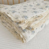 A stack of white floral muslin baby blankets with delicate lace trim, folded on a white surface.