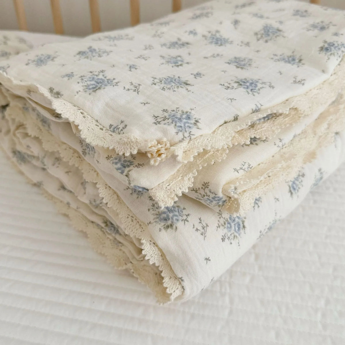 A stack of white floral muslin baby blankets with delicate lace trim, folded on a white surface.