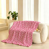 A pink leopard print flannel throw blanket draped on a white armchair next to a window.