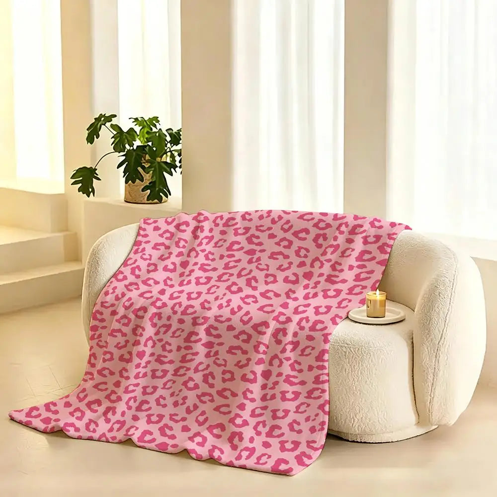 A pink leopard print flannel throw blanket draped on a white armchair next to a window.