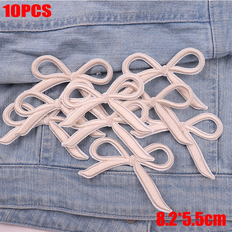 Ten embroidered light beige cartoon bow iron-on patches displayed on a denim fabric.