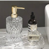 A clear glass soap dispenser with a gold pump and a small glass bottle are displayed on a clear tray.