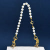 A pearl beaded necklace with a gold letter C charm displayed on a white quilted purse.