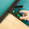 A hand holds a black multifunctional carpenter square with an angle level and protractor placed on a wooden surface next to a