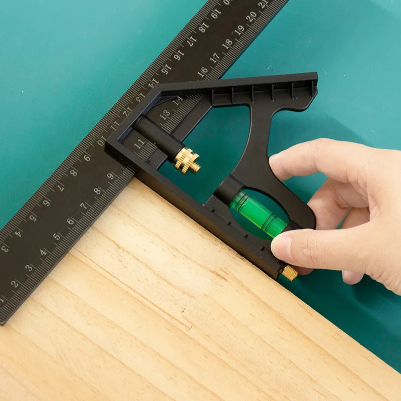 A hand holds a black multifunctional carpenter square with an angle level and protractor placed on a wooden surface next to a