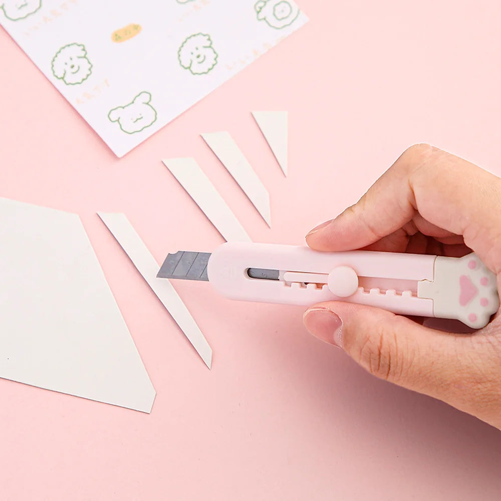 Eine Hand hält ein rosa Mini-Klaue-Werkzeugmesser mit Klinge neben weißen Papierfetzen.