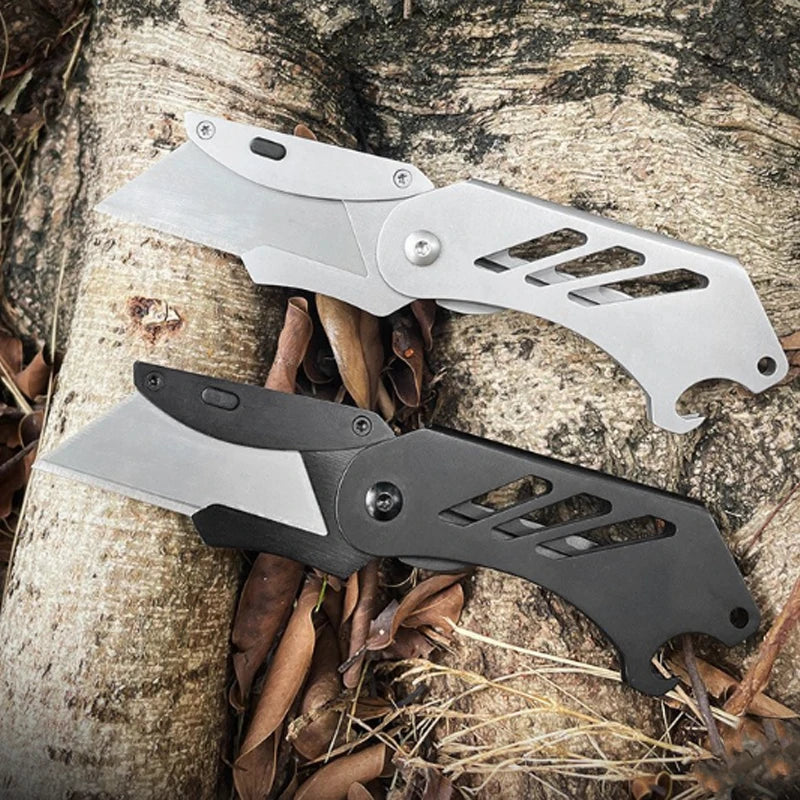 A stainless steel folding utility knife with five replaceable blades resting on a tree trunk amidst dry leaves.