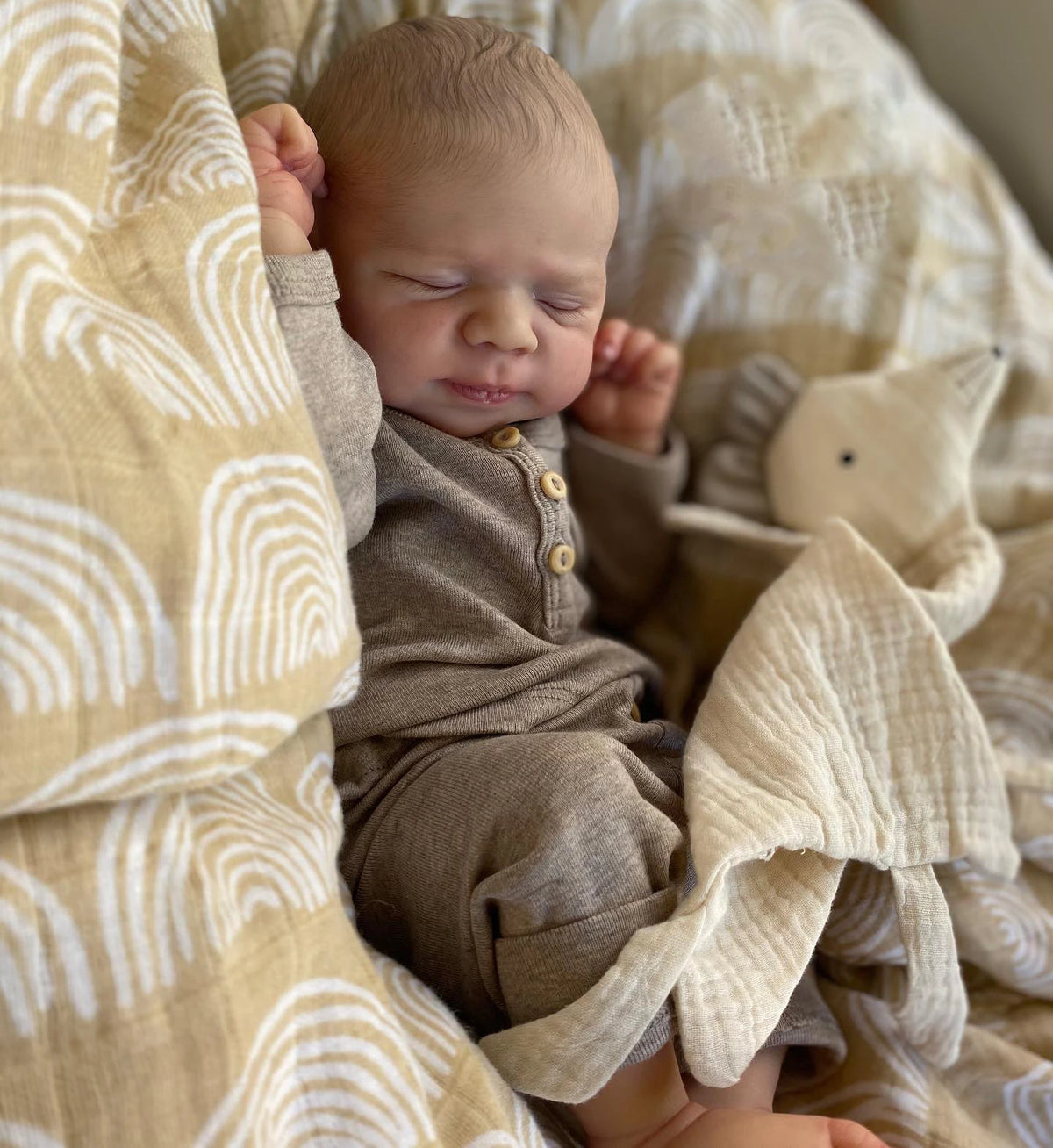 A newborn baby is sleeping in a light yellow and beige patterned fabric, wearing a brown outfit.