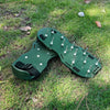 A pair of green adjustable lawn aerator shoes with heavy-duty spikes lying on green grass.