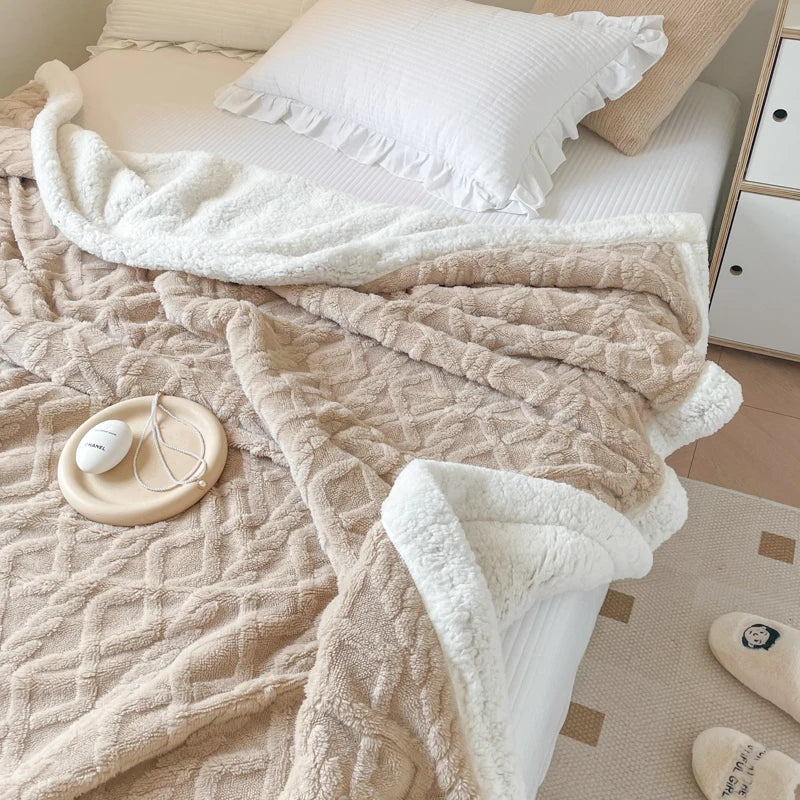 A beige double-layer fleece throw blanket draped over a white bed with a white pillow.