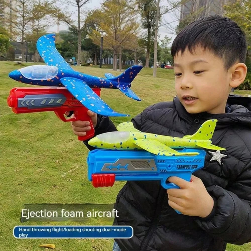 A boy holds a blue foam glider airplane and a red foam blaster, demonstrating the ejection foam aircraft toy set.