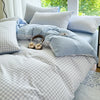 A light blue and gray striped duvet cover set with two pillows on a bed near a window.