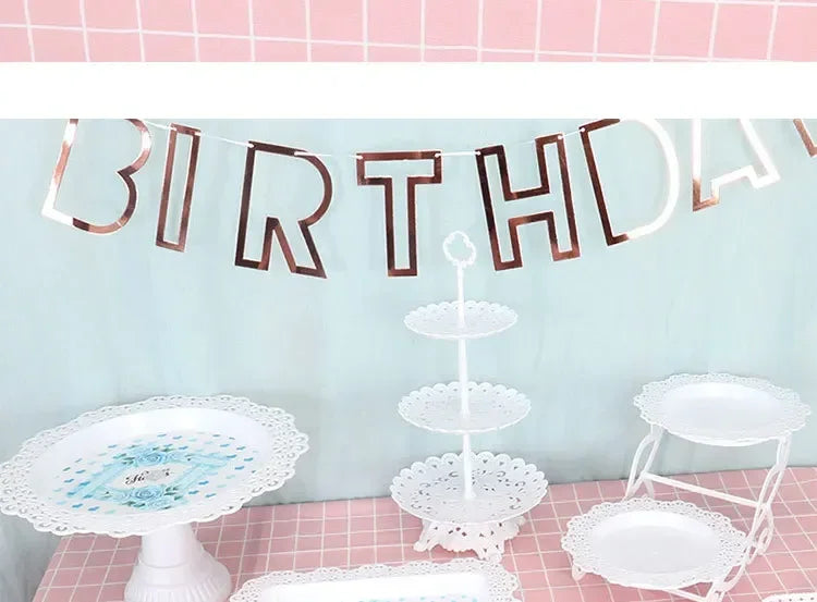 Dekorativer Banner mit 'birthday' auf blauer Wand, weiß und roségold und gestapelte weiße Plastikdeko
