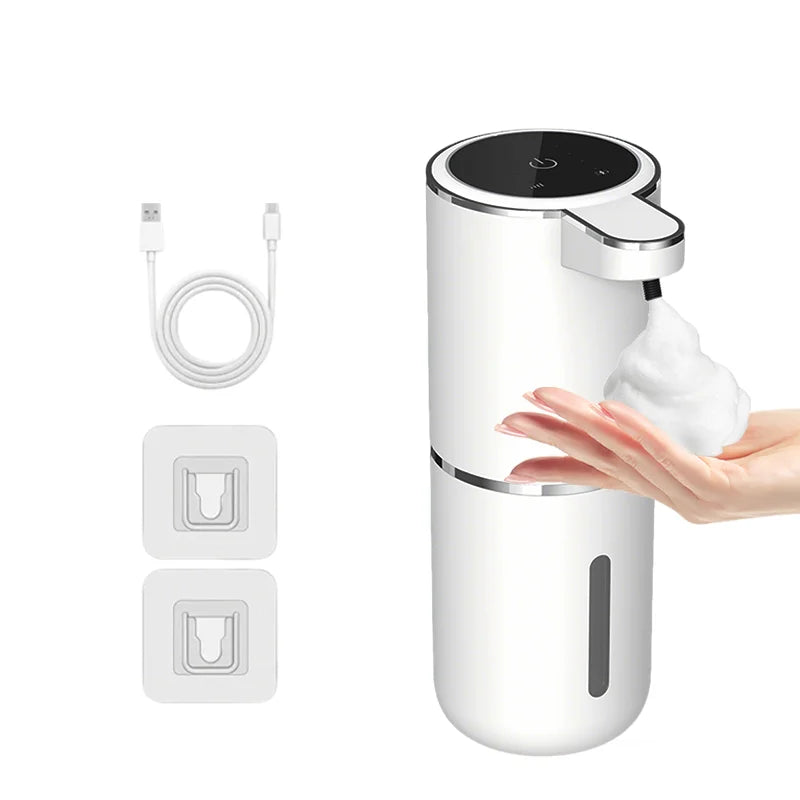 A white touchless automatic soap dispenser with a black top, shown next to its charging cable and replacement parts.