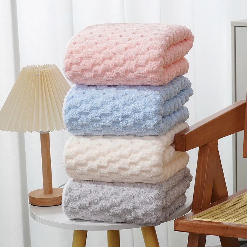 Stack of pink, blue, cream, and gray plush bath towels on a wooden surface.