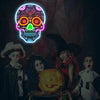 A group of children posing with a glowing skull-shaped LED neon light and a carved pumpkin.