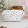 A white cosmetic pouch with a vintage rose print and delicate lace trim is displayed next to a woven basket.