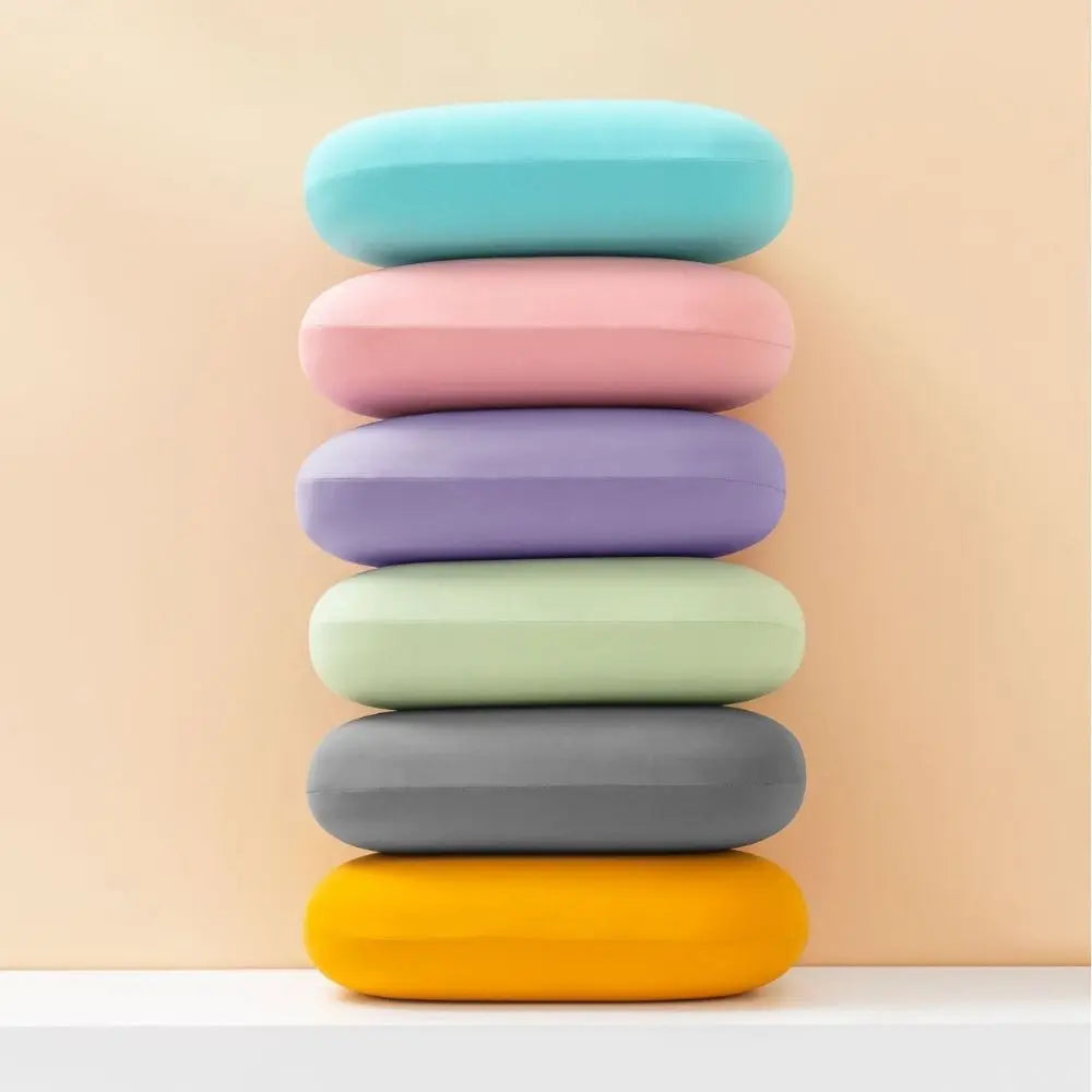 A stack of colorful memory foam travel neck pillows in pastel shades on a white shelf.