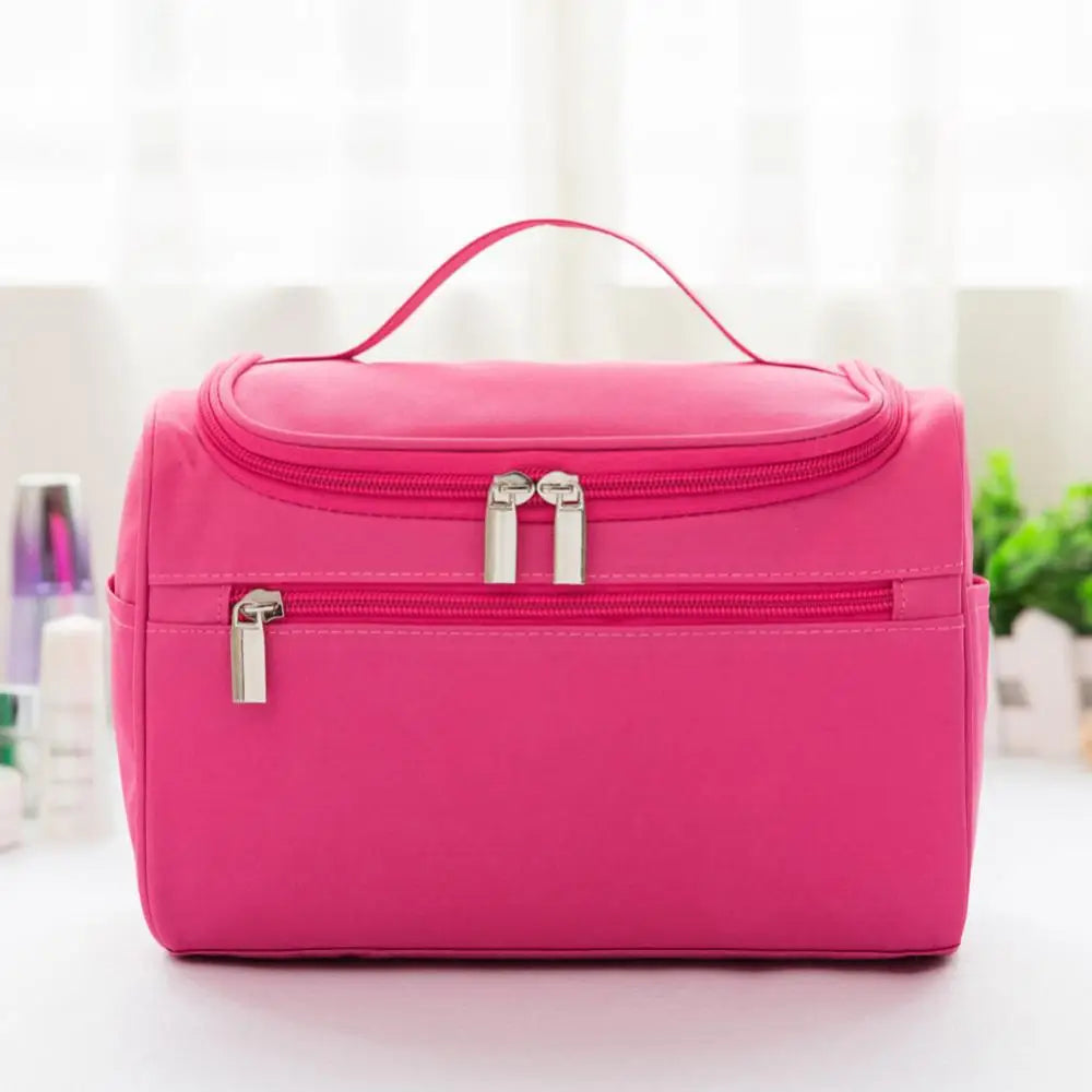 A bright pink hanging makeup bag with a zipper and metallic hardware is displayed on a white surface.