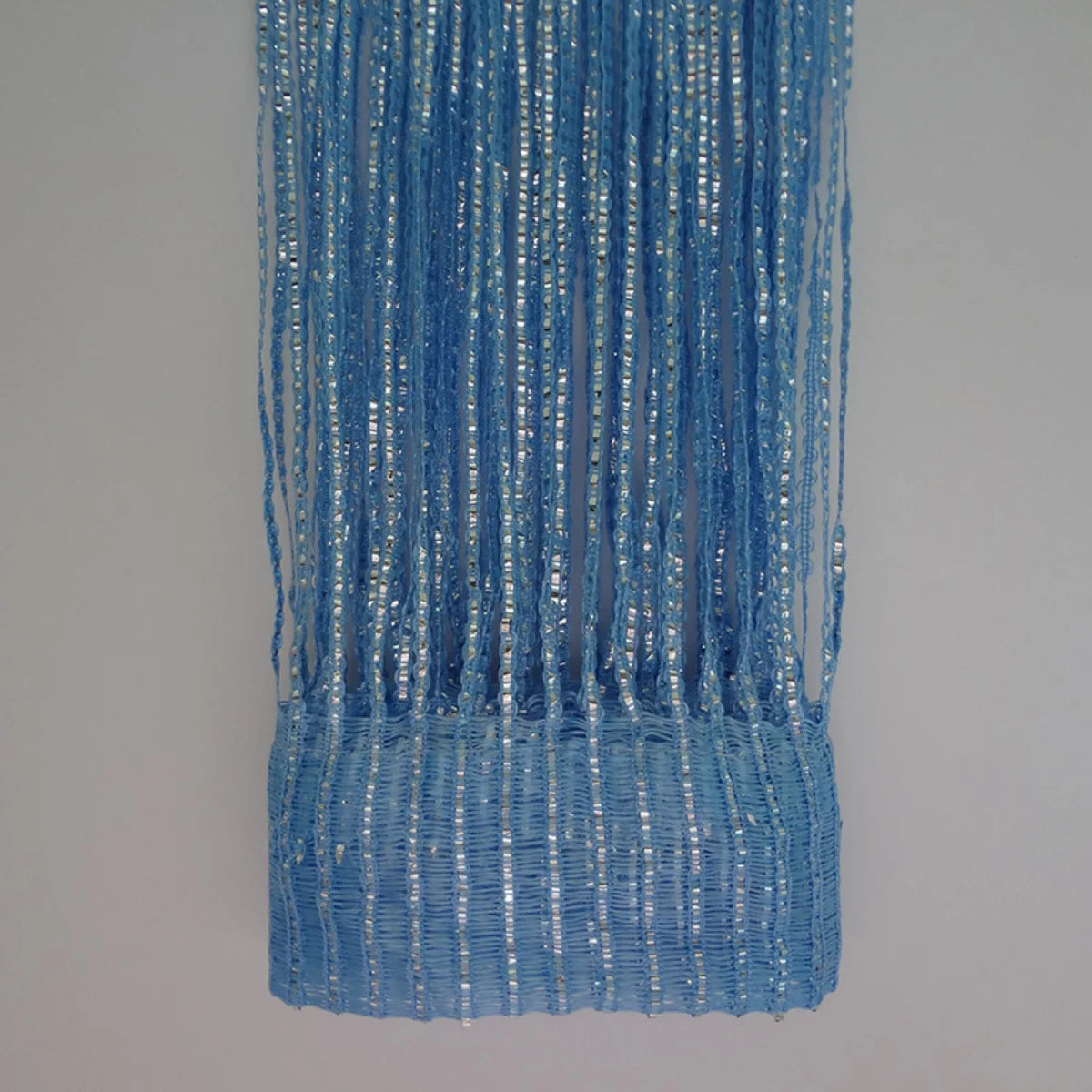 A vertical curtain made of blue and silver metallic tassels hanging against a light gray background.