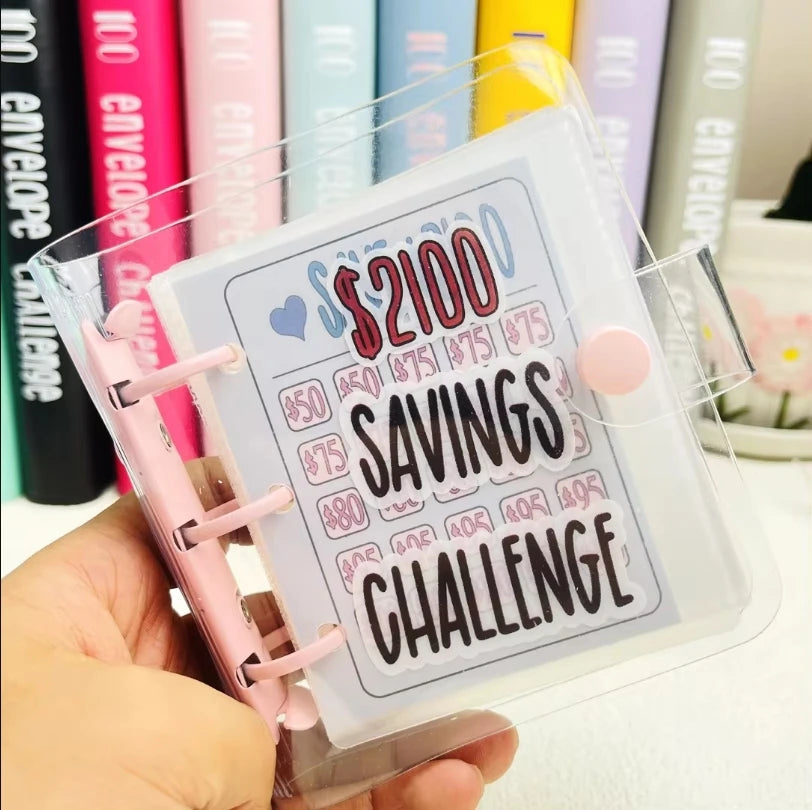 Eine Hand hält einen klaren Ordner mit der Aufschrift 'Savings Challenge' und Dollarbeträgen.