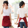 A woman models a classic half apron with pockets in maroon and black on a white t-shirt and jeans.