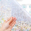 A hand touches a sheet of 3D rainbow privacy window film, showing stained glass decorative vinyl patterns.