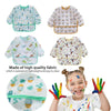 A child is wearing a colorful waterproof long sleeve art smock and feeding bib with various patterns.