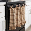 A plaid oven skirt in tan and brown tones with a ruffled trim hanging on a black stove.