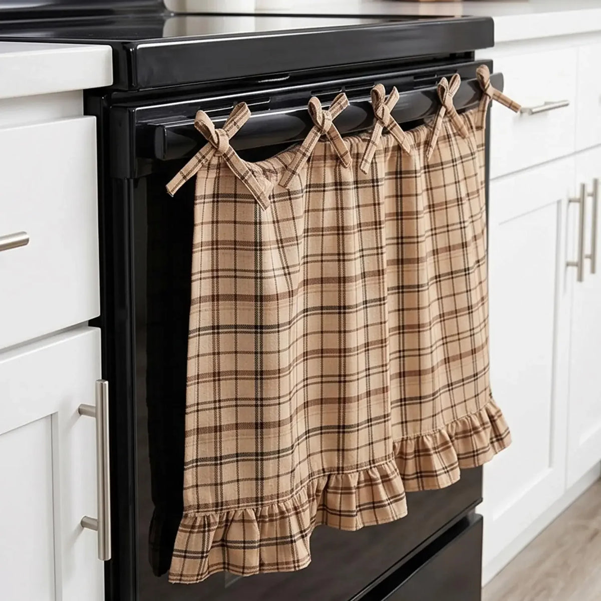 A plaid oven skirt in tan and brown tones with a ruffled trim hanging on a black stove.