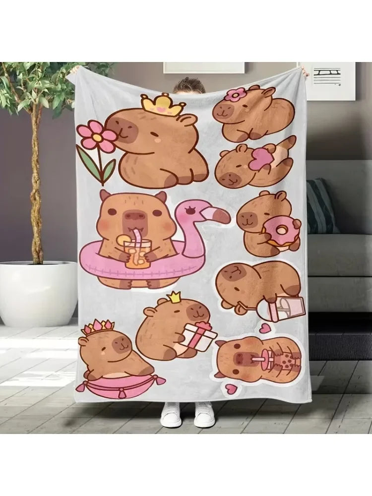 A beige flannel throw blanket featuring a repeating pattern of cute cartoon capybaras and a pink flamingo.