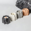 A collection of five candle holders made from textured silicone molds in shades of gray, beige, and black, set against a dark