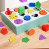 A wooden geometric shape and color sorting box filled with various colorful wooden shapes on a light wood surface.