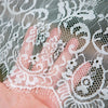 A hand is holding or touching white lace fabric featuring a French retro floral design.