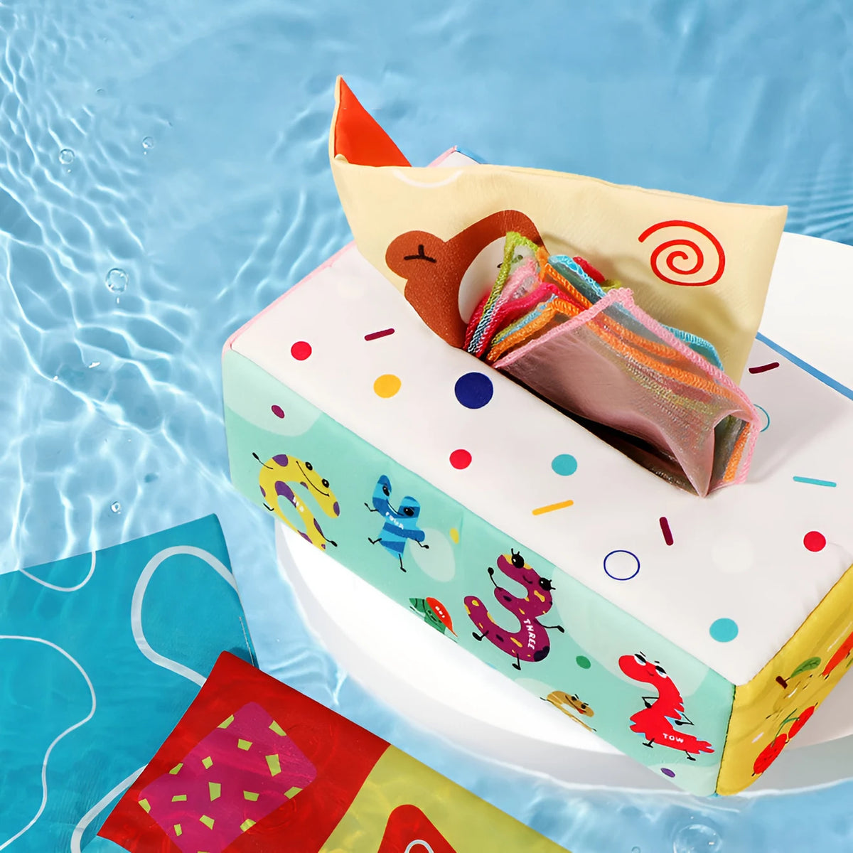 A colorful cloth book toy featuring cartoon animals and a ring for kids is displayed on water.