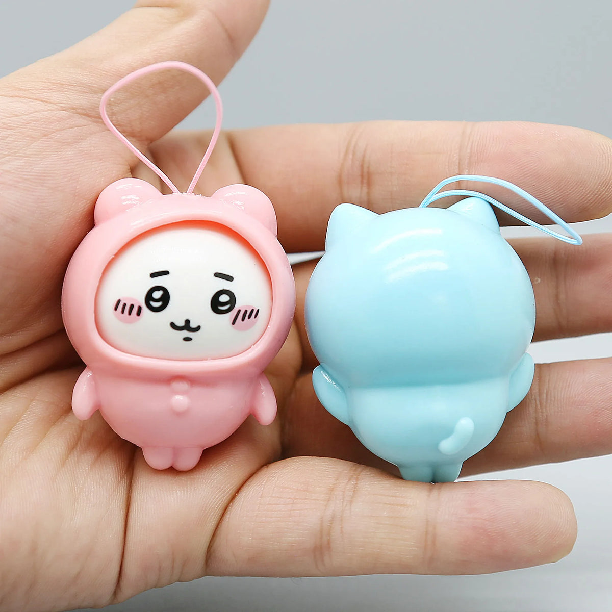 A pink Usagi and blue Hachiware PVC bag pendant doll are held in a person's hand.