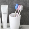 A white tube of tooth paste next to a white cup holding three colored silicone toothbrush heads.