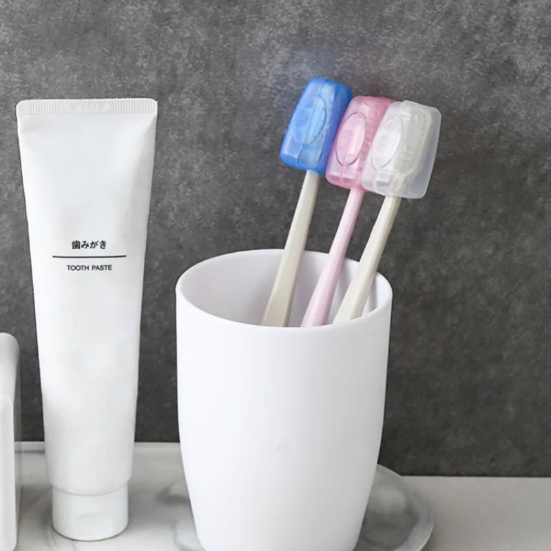 A white tube of tooth paste next to a white cup holding three colored silicone toothbrush heads.