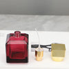 A red glass perfume bottle with a fine-mist sprayer and a gold-colored cap are displayed on a white surface.