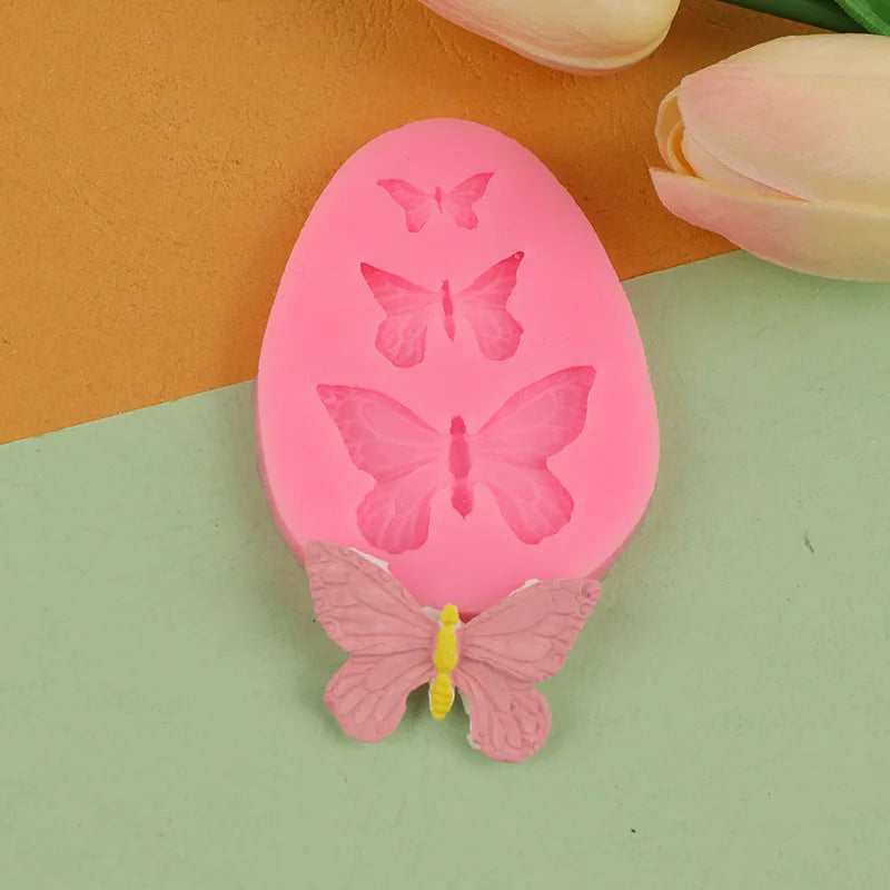 A pink silicone mold shaped like an egg with butterfly designs, resting on a green surface next to a pink tulip.