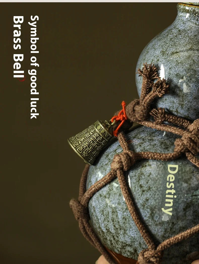 A close-up of a brass bell symbol for good luck attached to a blue ceramic gourd with a jute net bag.