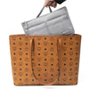 A hand is placing a gray travel season purse organizer insert into a brown leather handbag.