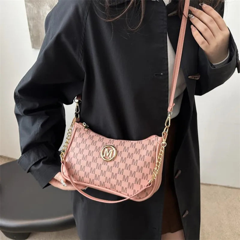 A woman holds a pink and white patterned PU leather crossbody bag with a gold chain strap against a black coat.
