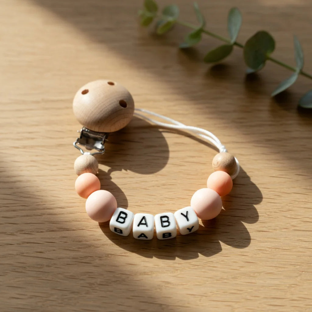 A wooden baby pacifier clip with a white cord and a name tag spelling out BABY