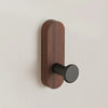 A dark brown walnut wood hook mounted on a light wall, used for entryway or bathroom organization.